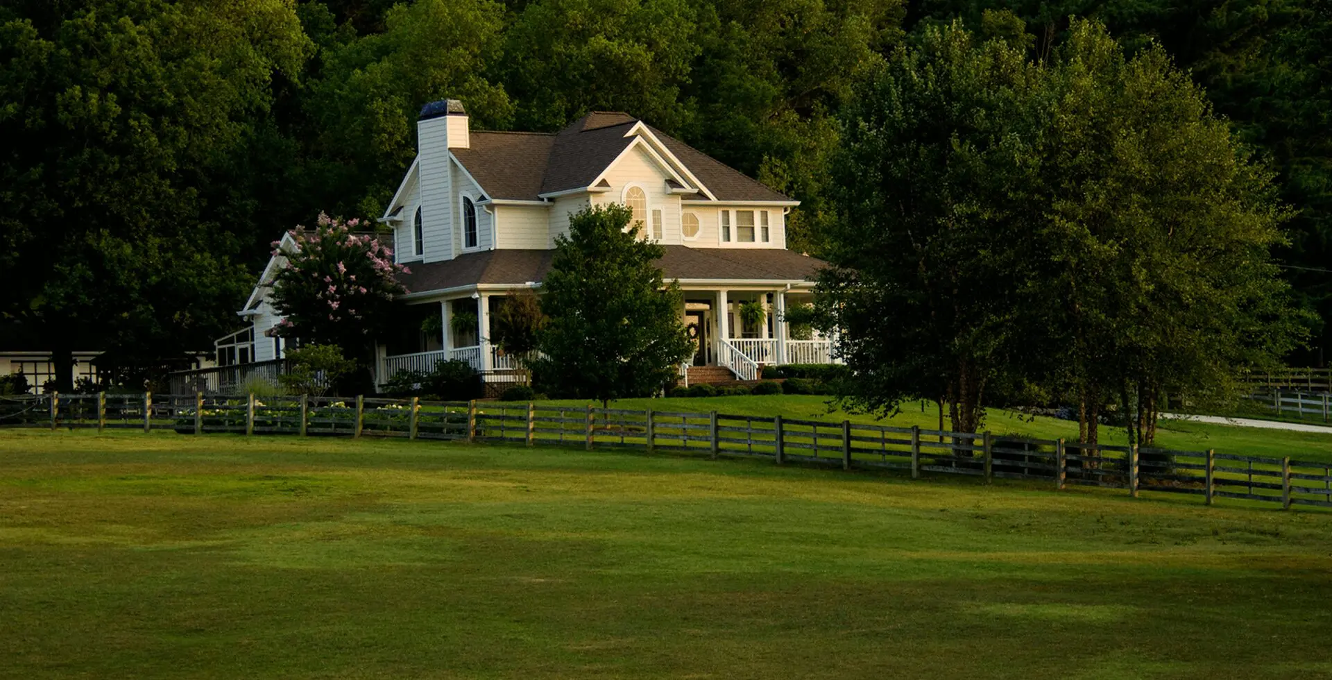 the beautiful massive house is surrounded by trees, and the in front of the house is a large grassy area.